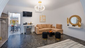 Een moderne woonkamer met een beige bank, een salontafel en een aan de muur bevestigde televisie. Er staat een klein tafeltje met een paar spullen op, en er is een stoel in de achtergrond zichtbaar.