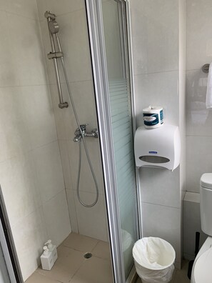 A shower with a glass door, a toilet, and a hand soap dispenser. - Guesthouse Inciti (Kowloon)