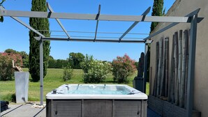 Ein Whirlpool unter einer Pergola mit einer Holzterrasse und Steinen darumherum.