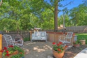 An outdoor patio with two white metal chairs, a wooden table, and potted plants.