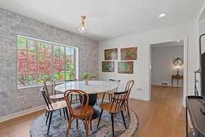 A dining area with a round table and chairs, a brick wall, and a large window with a view of trees. - Beautiful Villa Leocadia+ Private Pool + Sleeps 8! (Kansas City)