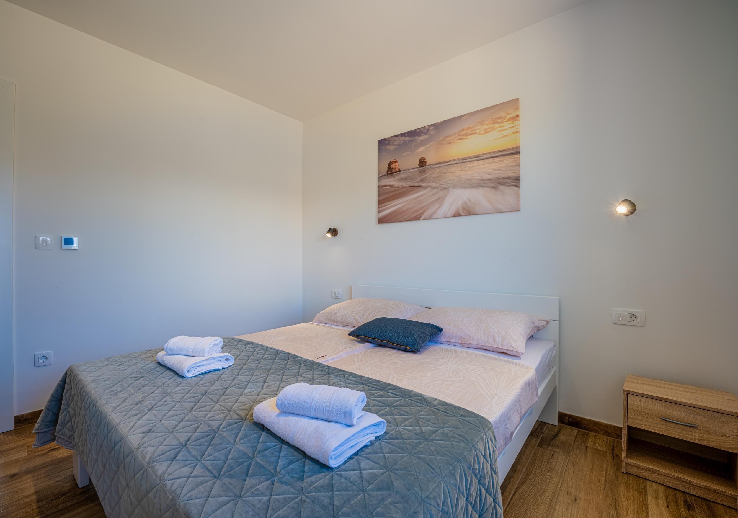 A neatly made bed with a quilted bedspread, a pillow, and folded towels.