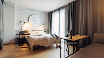 Ein modernes Hotelzimmer mit Bett, Nachttisch, Laptop, einer Weinflasche und Blick ins Freie.