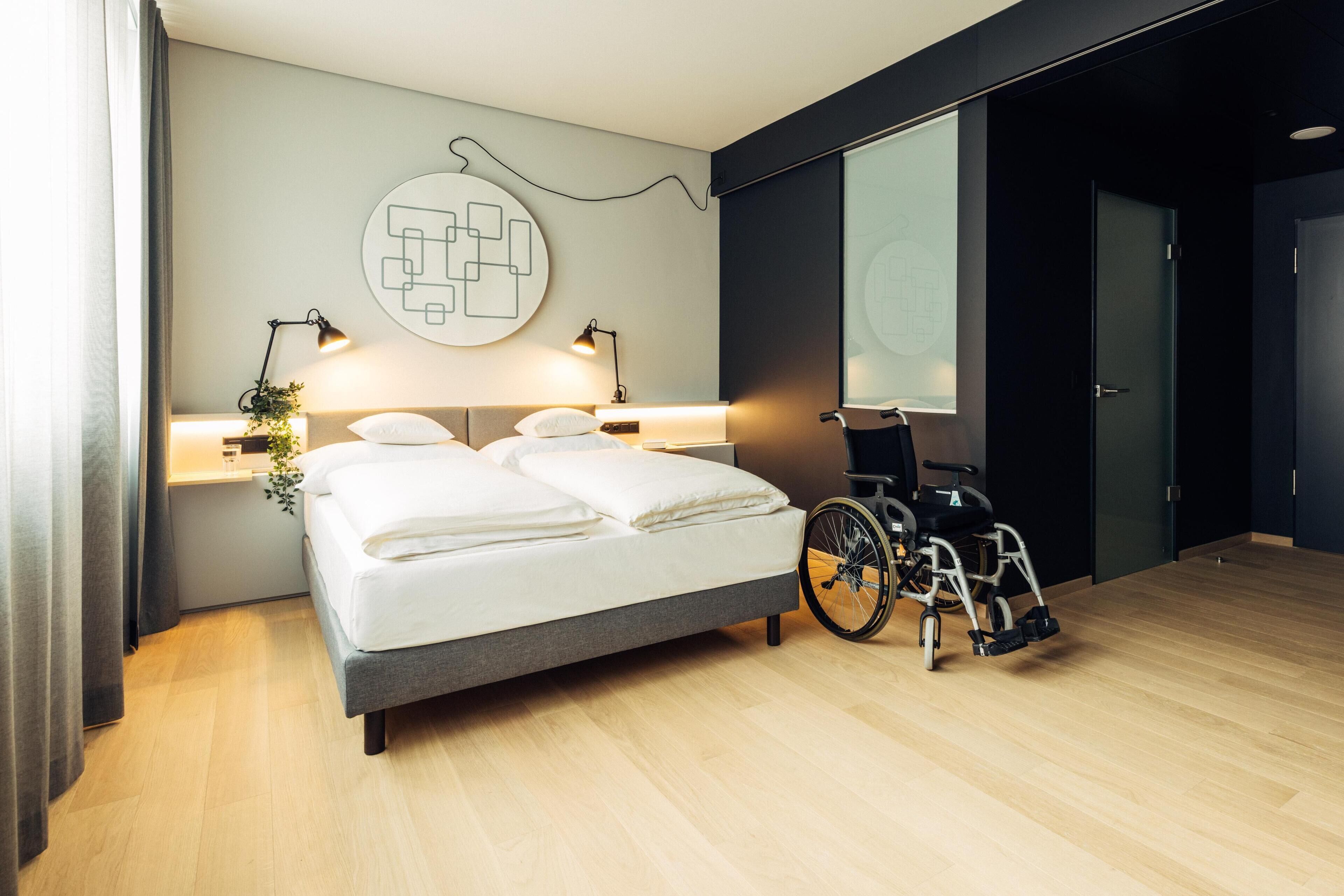 Un dormitorio moderno con una cama grande, lámparas de noche, una silla de ruedas y un proyector fijado a la pared.