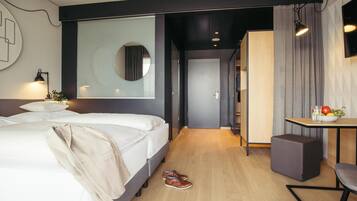 Una habitación de hotel moderna con una cama grande, una mesita de noche con un cuenco de fruta, un espejo y un escritorio con una silla.