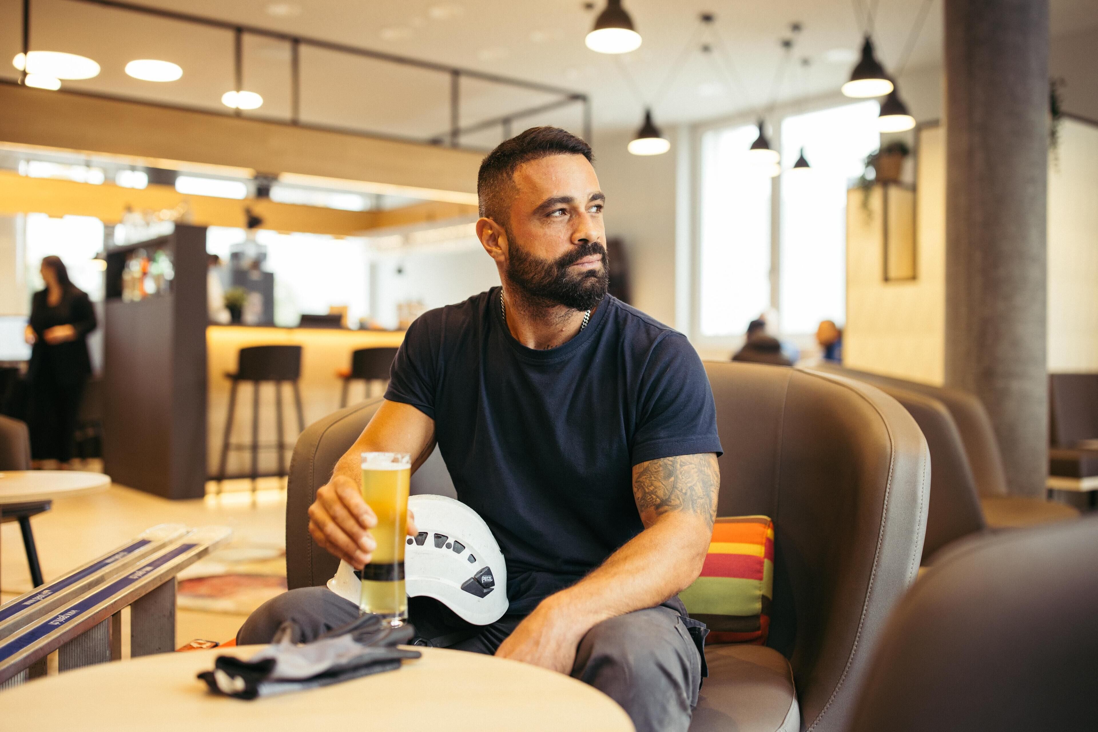 Um homem sentado em uma área de estar moderna com assentos de couro, um bar ao fundo e uma atmosfera relaxada.