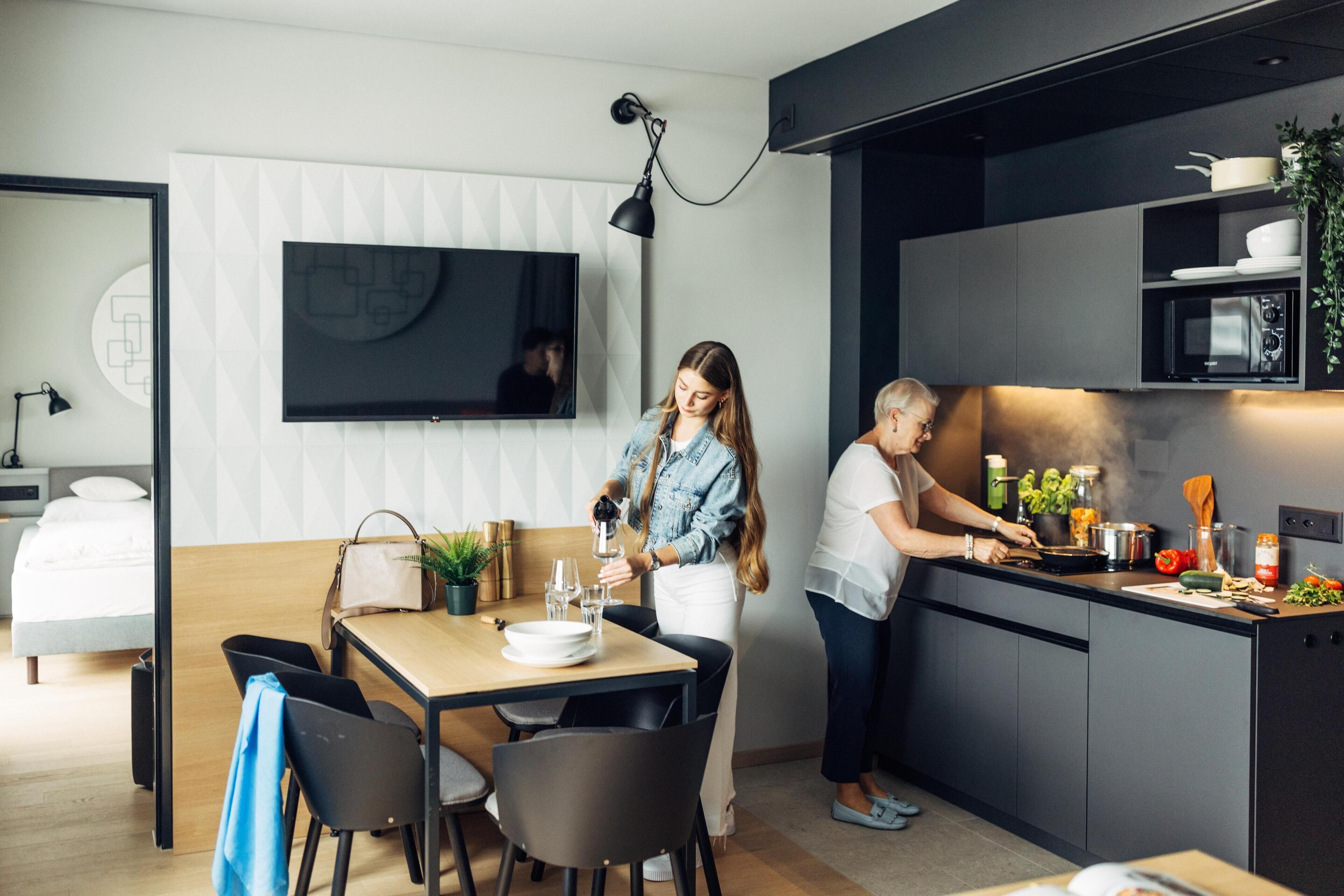 A modern kitchen with a dining area, a flat-screen TV mounted on the wall, and a small dining table with chairs.