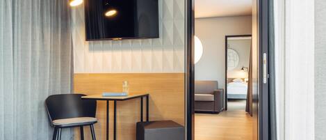 Habitación de hotel con cama, escritorio con silla, televisión montada en la pared y una pequeña mesa con un vaso.