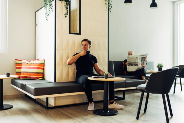 A modern lounge area with a sofa, a small table with a laptop, and a chair. - harry’s home Zürich-Limmattal (Spreitenbach)