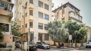 A multi-story building with balconies, parked cars, and a tree in front. - Mamad Relaxed Beachside Living | Cozy 2BR (Tel Aviv-Yafo)