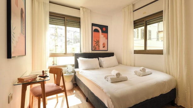 A hotel room with a bed, a desk, a chair, and a window with curtains. - Mamad Relaxed Beachside Living | Cozy 2BR (Tel Aviv-Yafo)