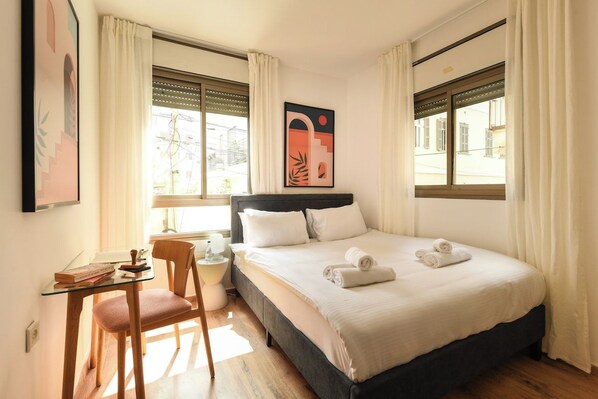 A hotel room with a bed, a desk, a chair, and a window with curtains.