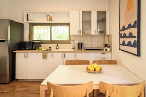 A modern kitchen with white cabinets, a stainless steel refrigerator, and a dining table with wooden chairs.