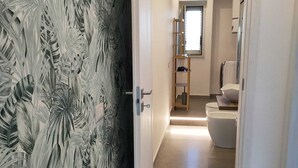 A hallway with a door featuring a tropical leaf pattern, leading to a bathroom with a toilet and a sink. - the garden of Etna (Mascalucia)
