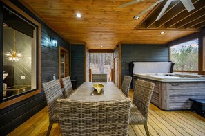 Une charmante cabane en bois dotée d’un coin repas avec des chaises en osier et d’un bain à remous.