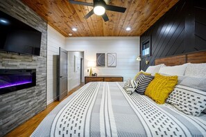 Une chambre à coucher avec un lit, une télévision, une cheminée et un ventilateur de plafond.