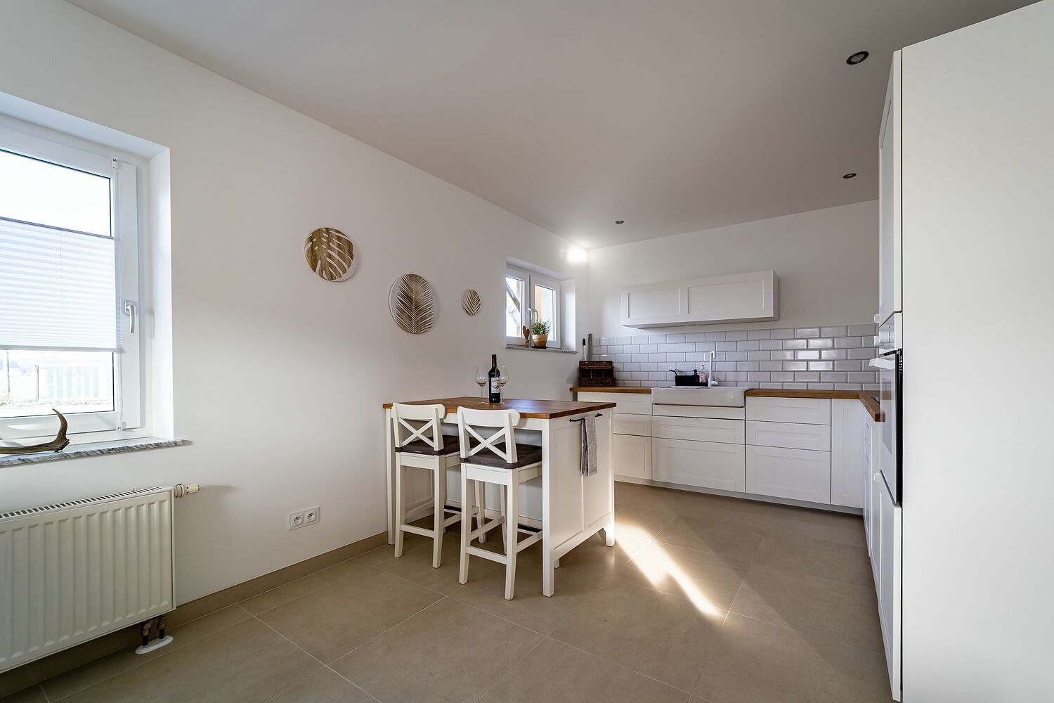 A modern kitchen with white cabinets, a wooden countertop, and a small dining area with two chairs.