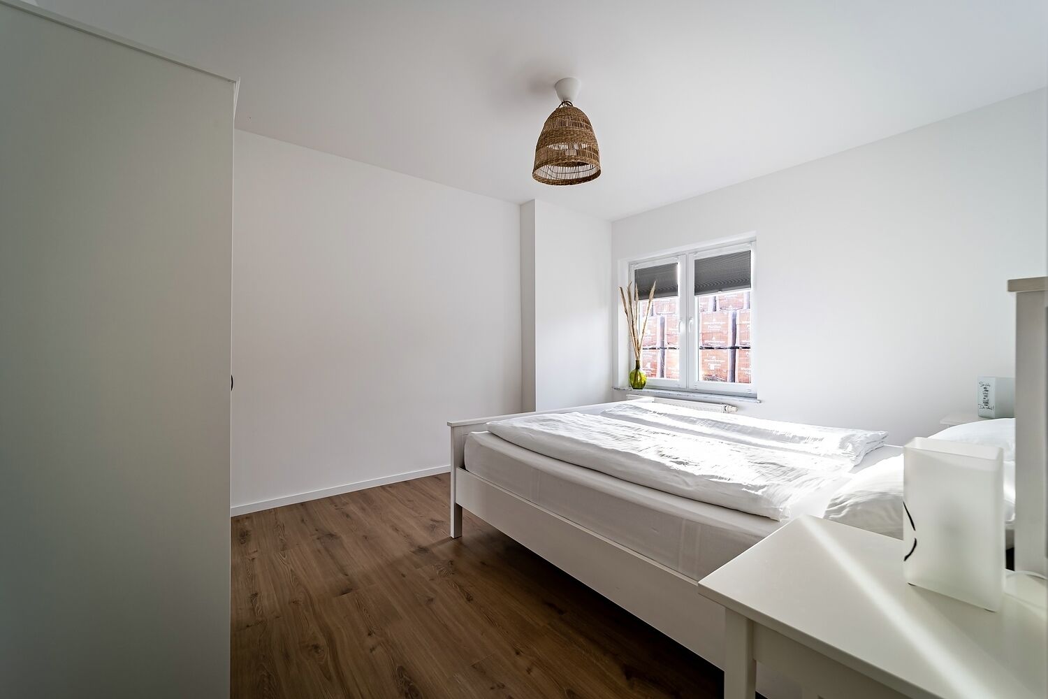 A bedroom with a bed, a window with a view, a bedside table, and a hanging light fixture.