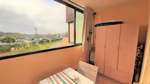 A balcony with a table set for two, a wardrobe, and a view of a parking lot and buildings. - Ideal studio near beach and port, sleeps 3 (Capbreton)