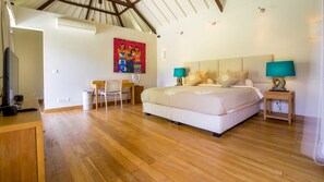 Une chambre avec un grand lit, deux tables de chevet avec des lampes, un bureau avec une chaise, un tableau au mur et un plancher en bois.