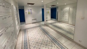Un couloir avec des casiers, un sol carrelé et un grand miroir qui reflète l’espace.