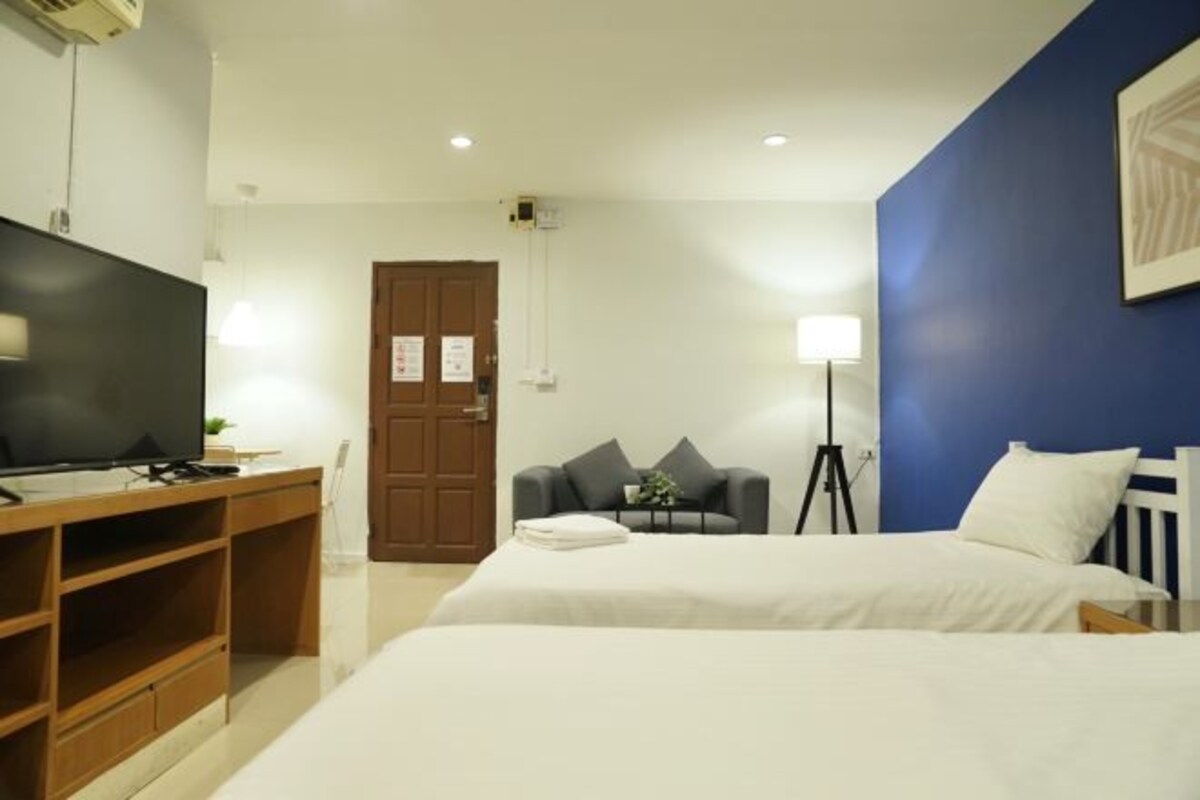 A hotel room with two beds, a desk with a flat-screen TV, a lamp, and a door.