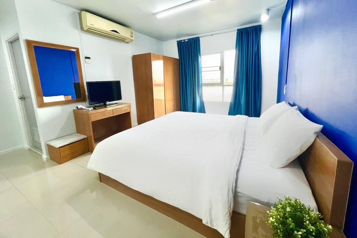 A hotel room with a large bed, a desk with a computer, a mirror, and a window with curtains.
