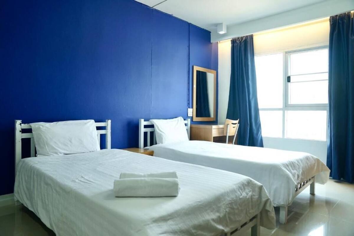 A hotel room with two beds, a desk, a chair, a window with curtains, and a mirror on the wall.