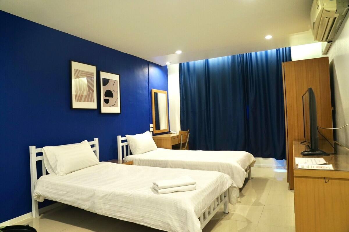 A hotel room with two beds, a desk, a chair, a mirror, and a television.