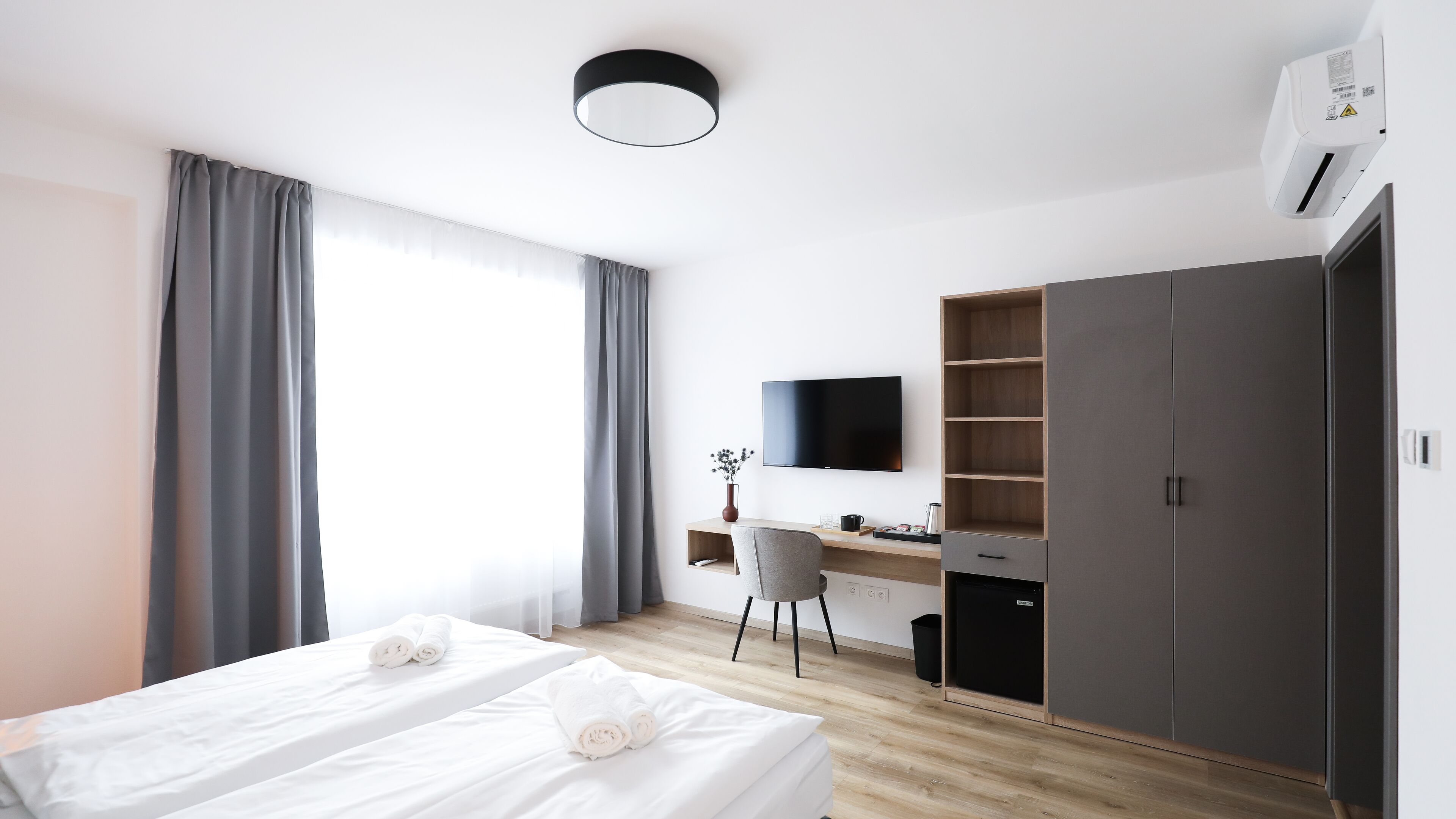 Una habitación de hotel moderna con una cama, un escritorio, una silla, un armario y un televisor.