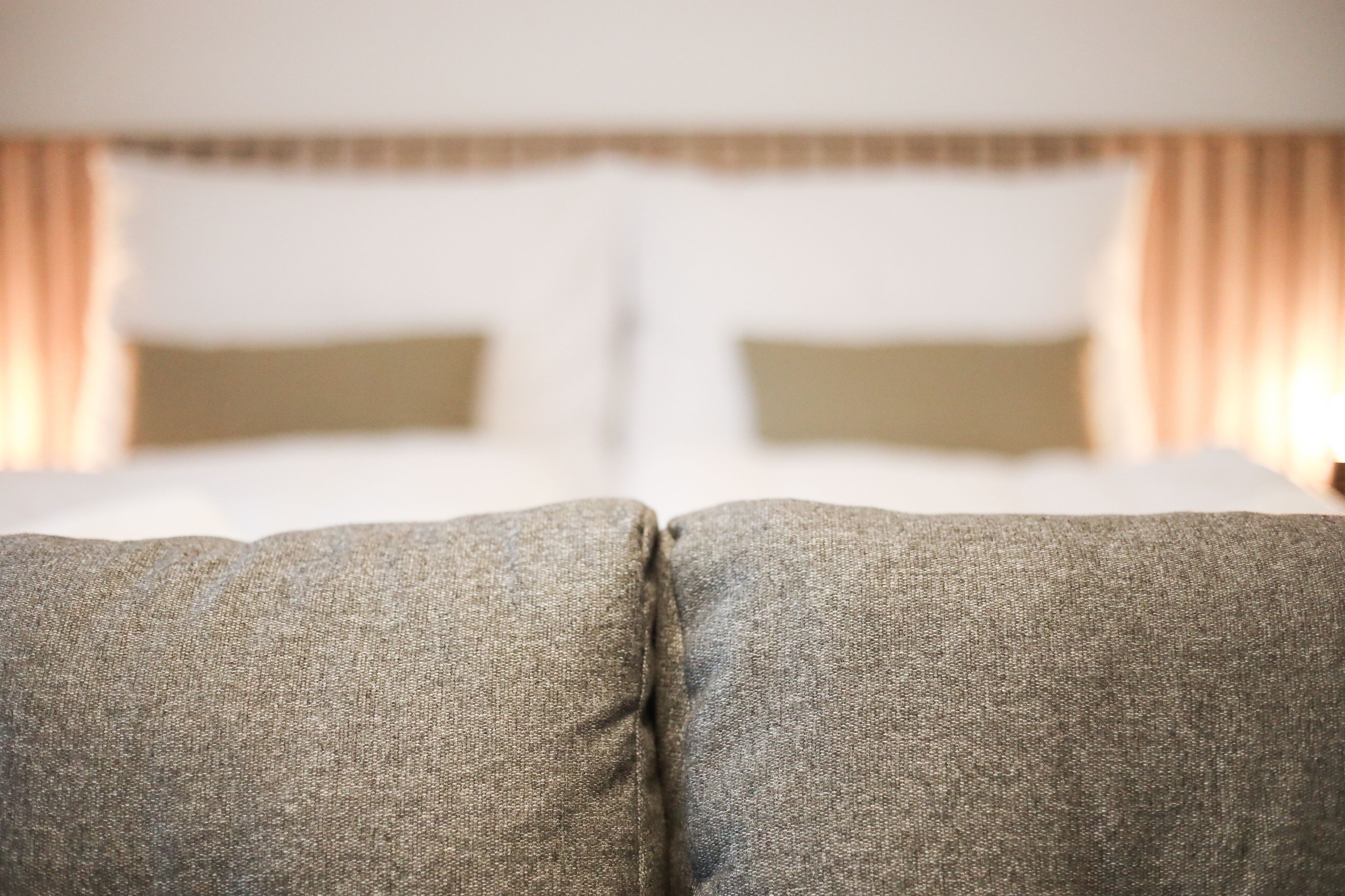 Primer plano de un sofá de tela texturizada, ubicado frente a una cama con cabecera y cortinas.