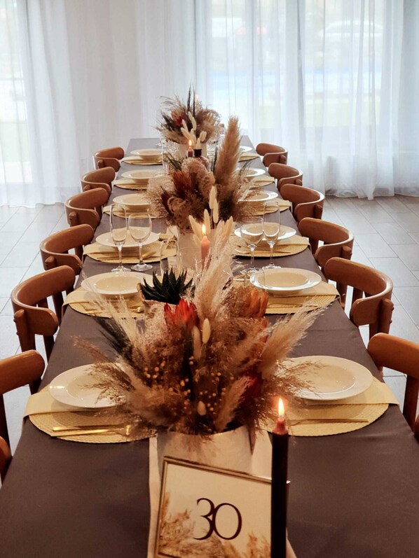 Una larga mesa de comedor preparada para 30 personas, con un número, velas y follaje decorativo.