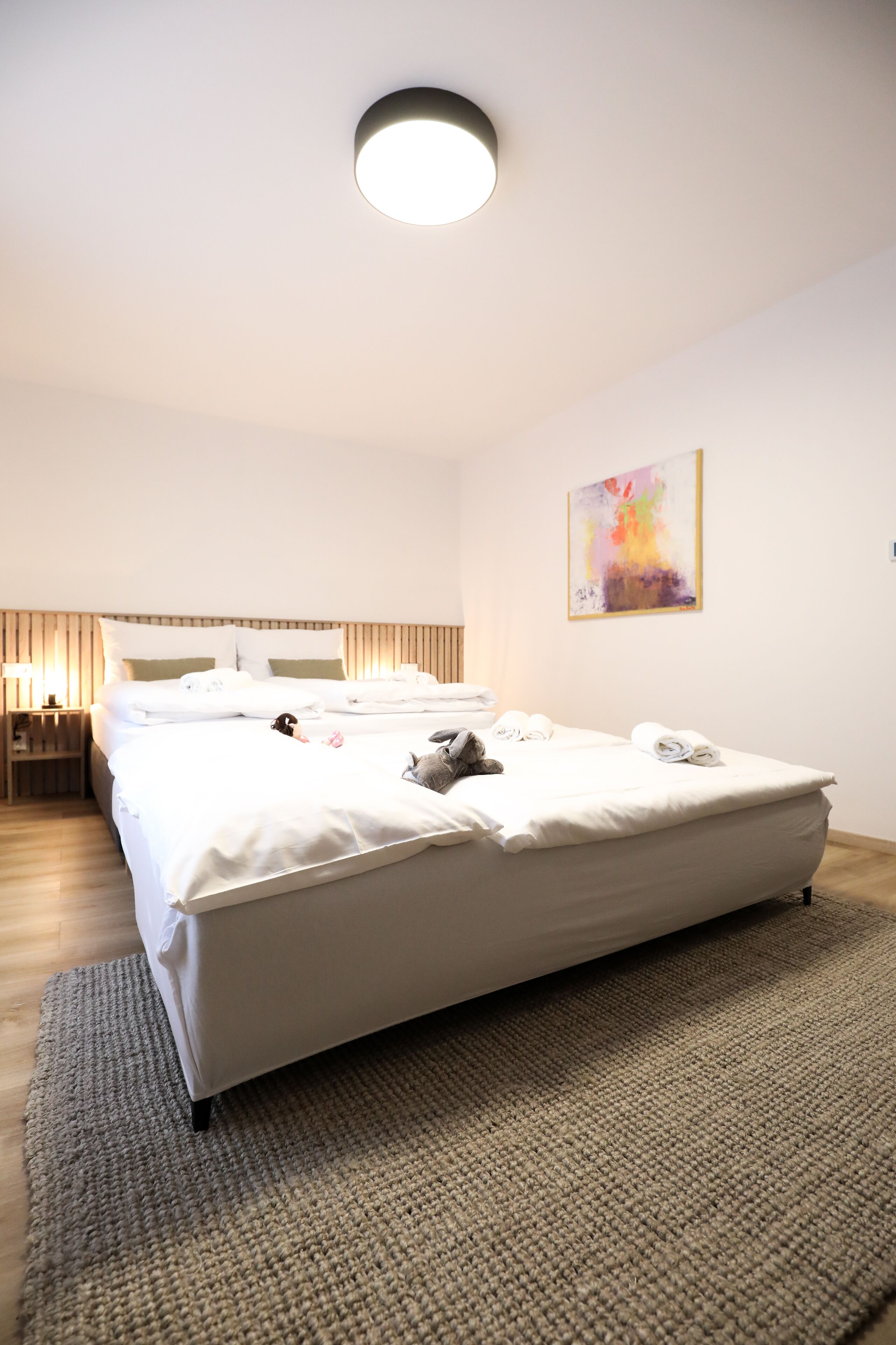 Una habitación de hotel moderna con una cama grande, una mesita de noche, una lámpara y un cuadro en la pared.