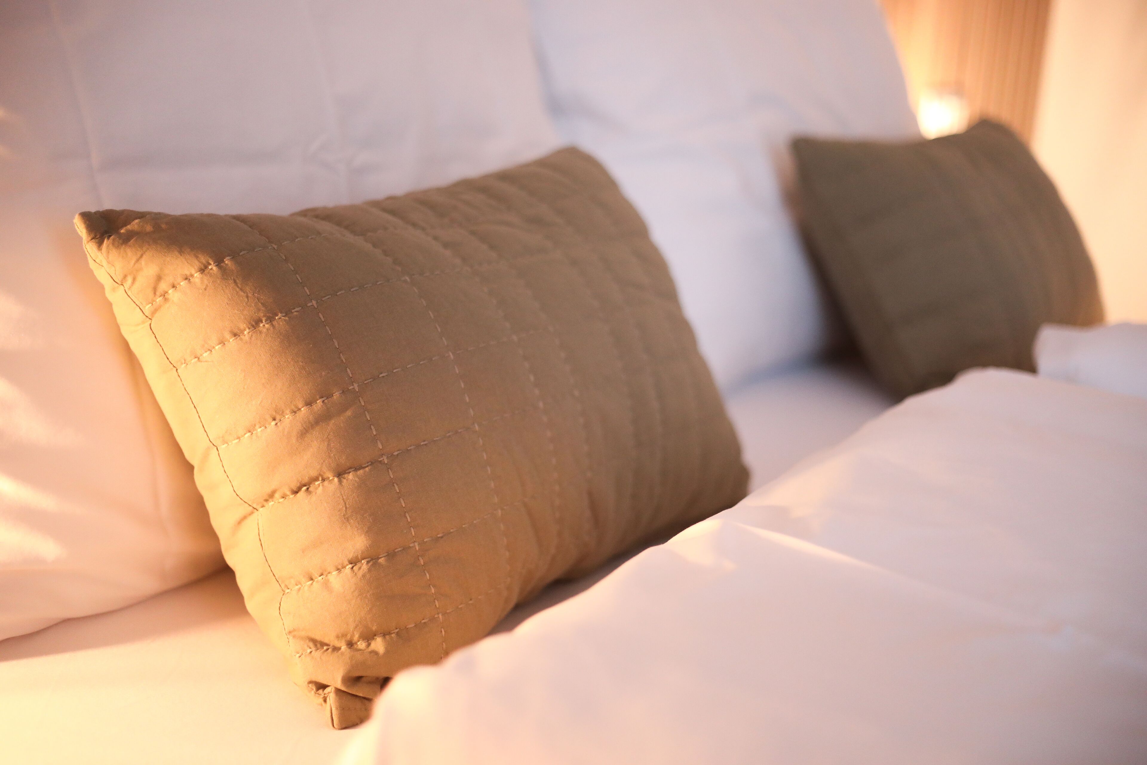 A bed with white bedding and two pillows, one beige and one green.