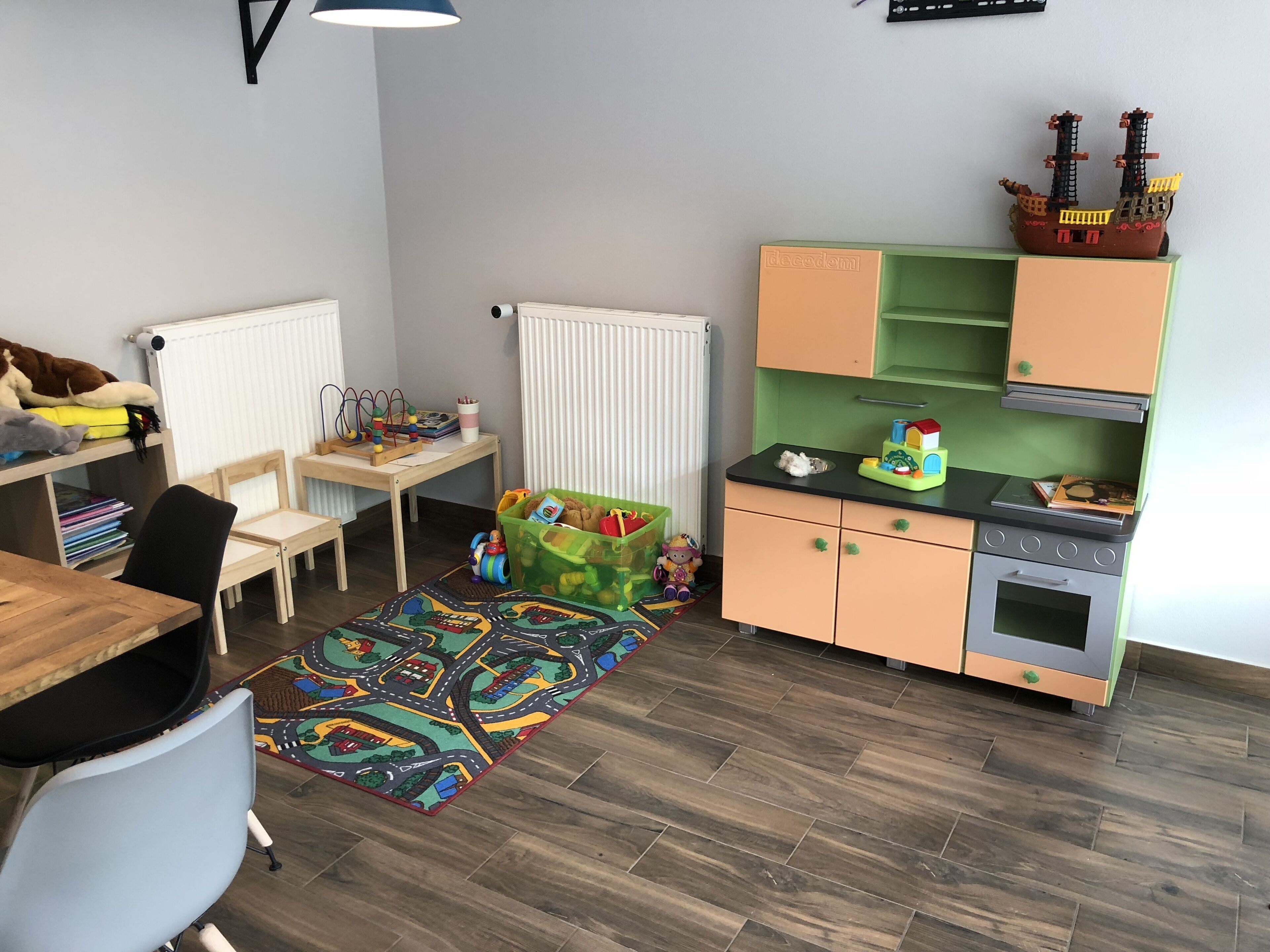 A child's playroom with a desk, chairs, a play mat, a toy ship, and a small kitchenette.