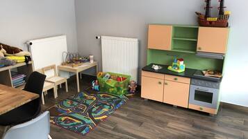 A child's playroom with a desk, chairs, a play mat, a toy ship, and a small kitchenette.
