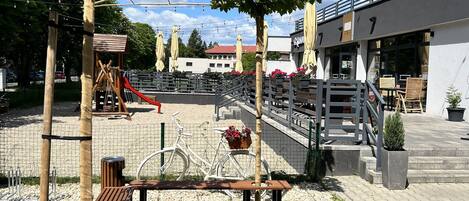 Un parque infantil con tobogán, estructuras para escalar y un área cercada. Hay un banco y una bicicleta.
