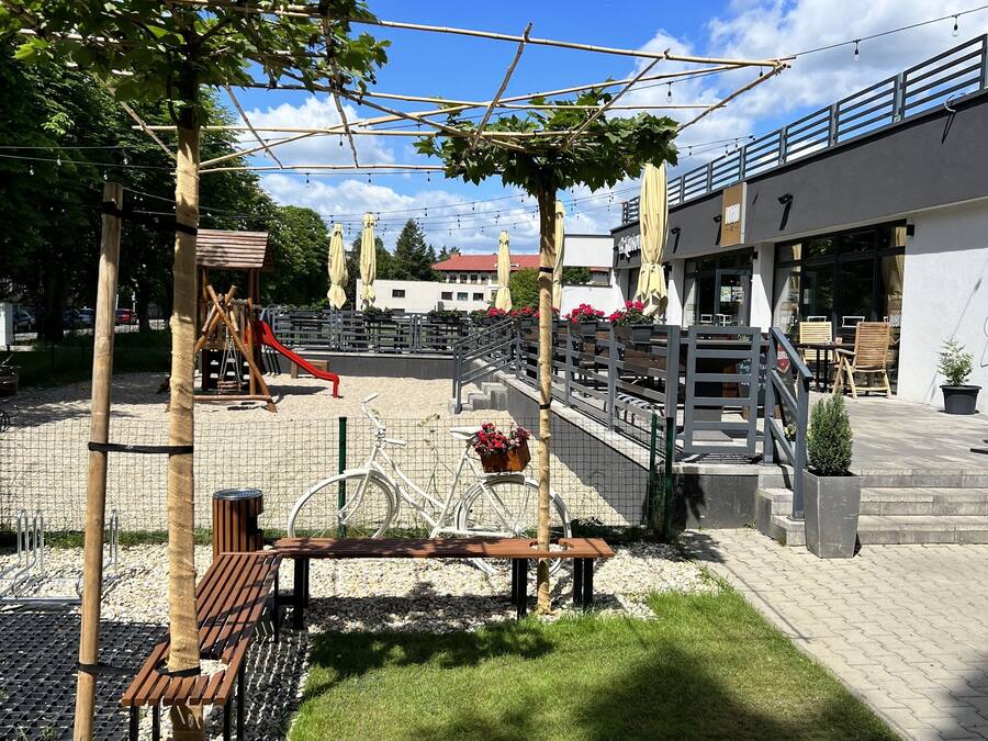 A playground with a slide, climbing structures, and a fenced area. There is a bench and a bicycle.