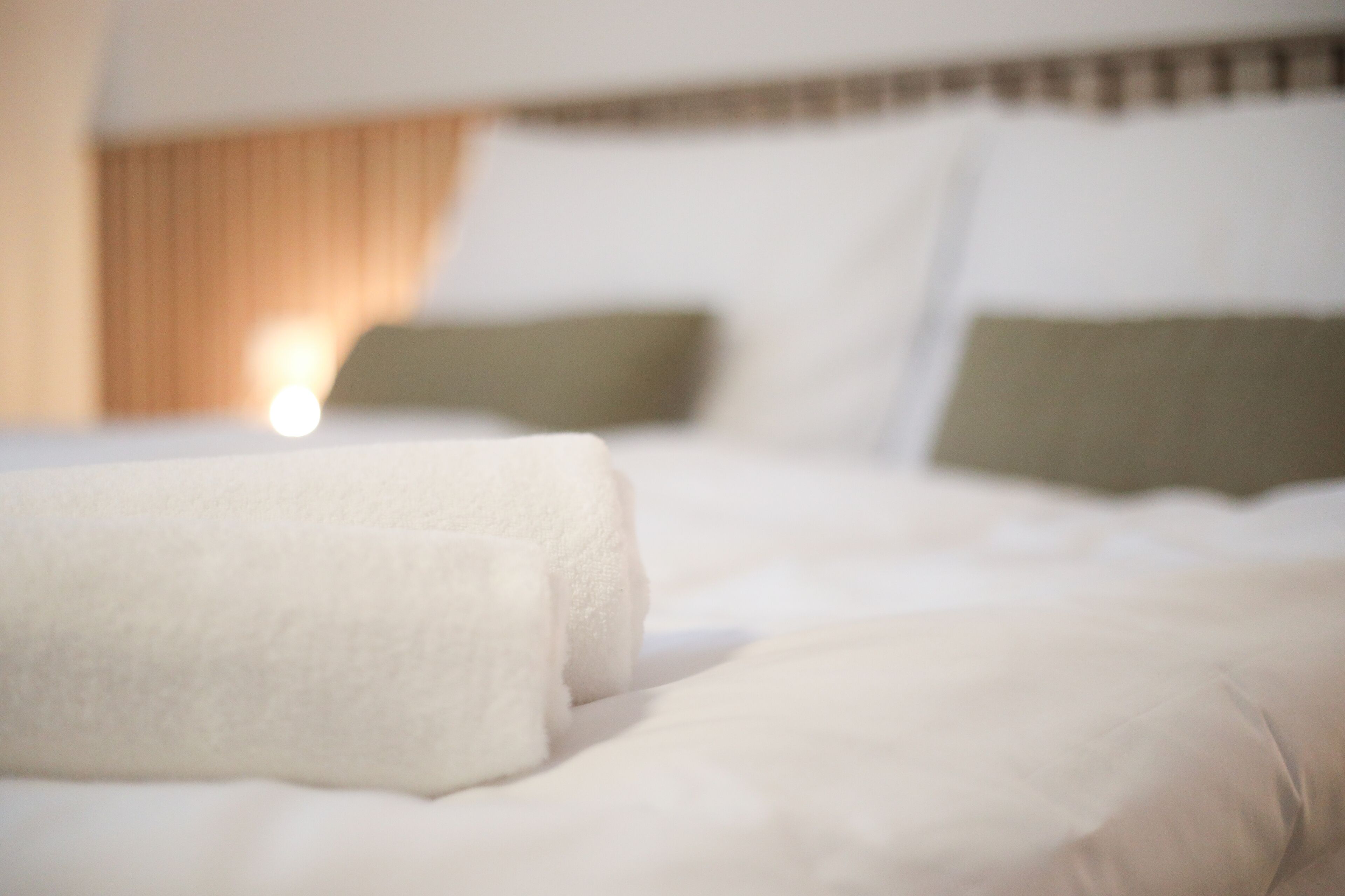 A bed with white linens and two pillows, one green and one white, in a hotel room.
