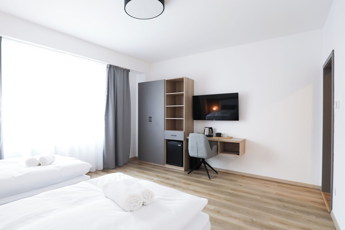 Ein Hotelzimmer mit zwei Betten, einem Fernseher, einem Schreibtisch mit Stuhl und einem Kleiderschrank.