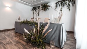 A room with a long table covered with a grey cloth, decorated with candles and greenery.