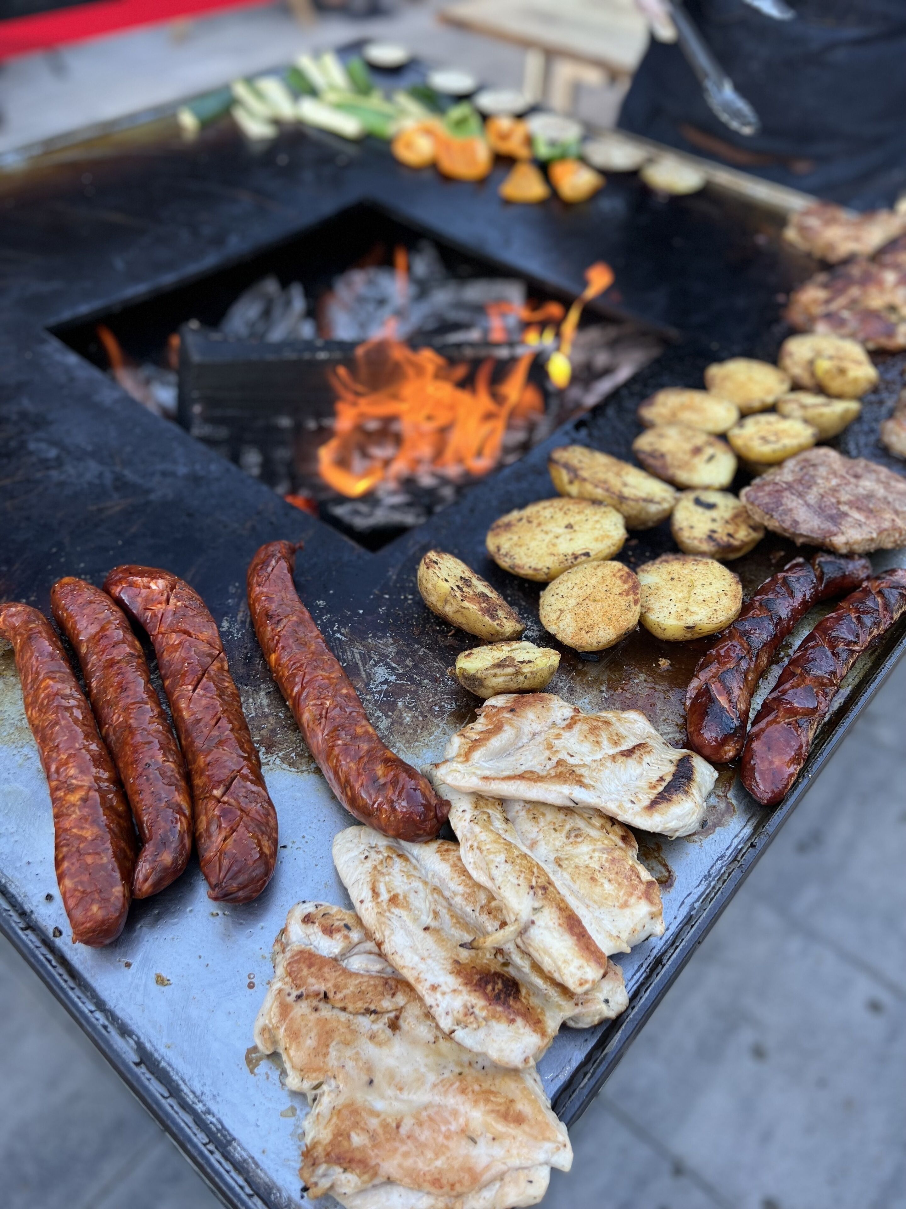 A grill with sausages, potatoes, and grilled meat.