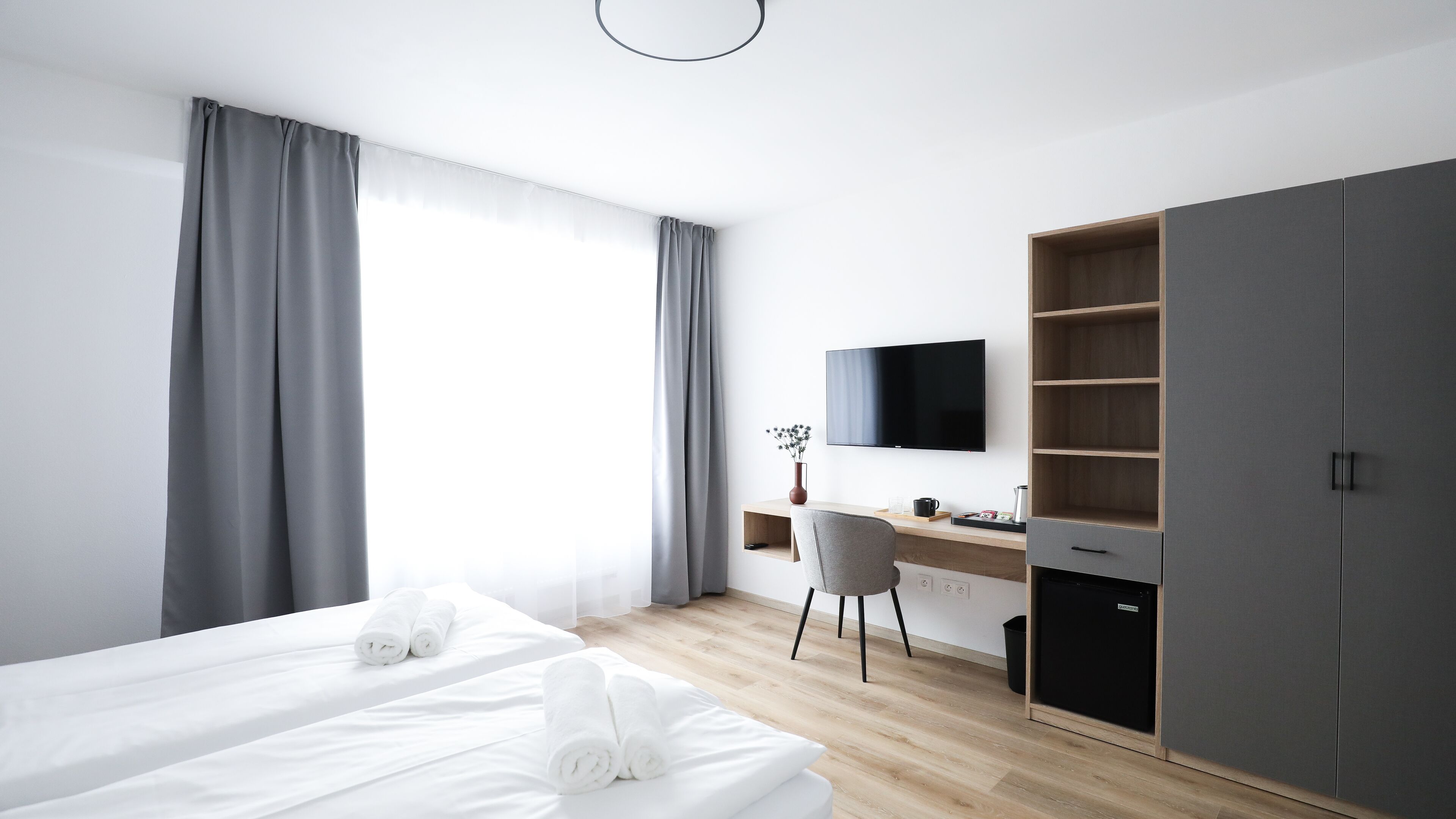 Una habitación de hotel moderna con cama, escritorio, silla, televisor y armario.