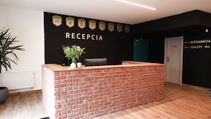 A reception desk with a brick counter, a potted plant, and a wall with icons indicating amenities like a bed, dining, and bicycle parking.