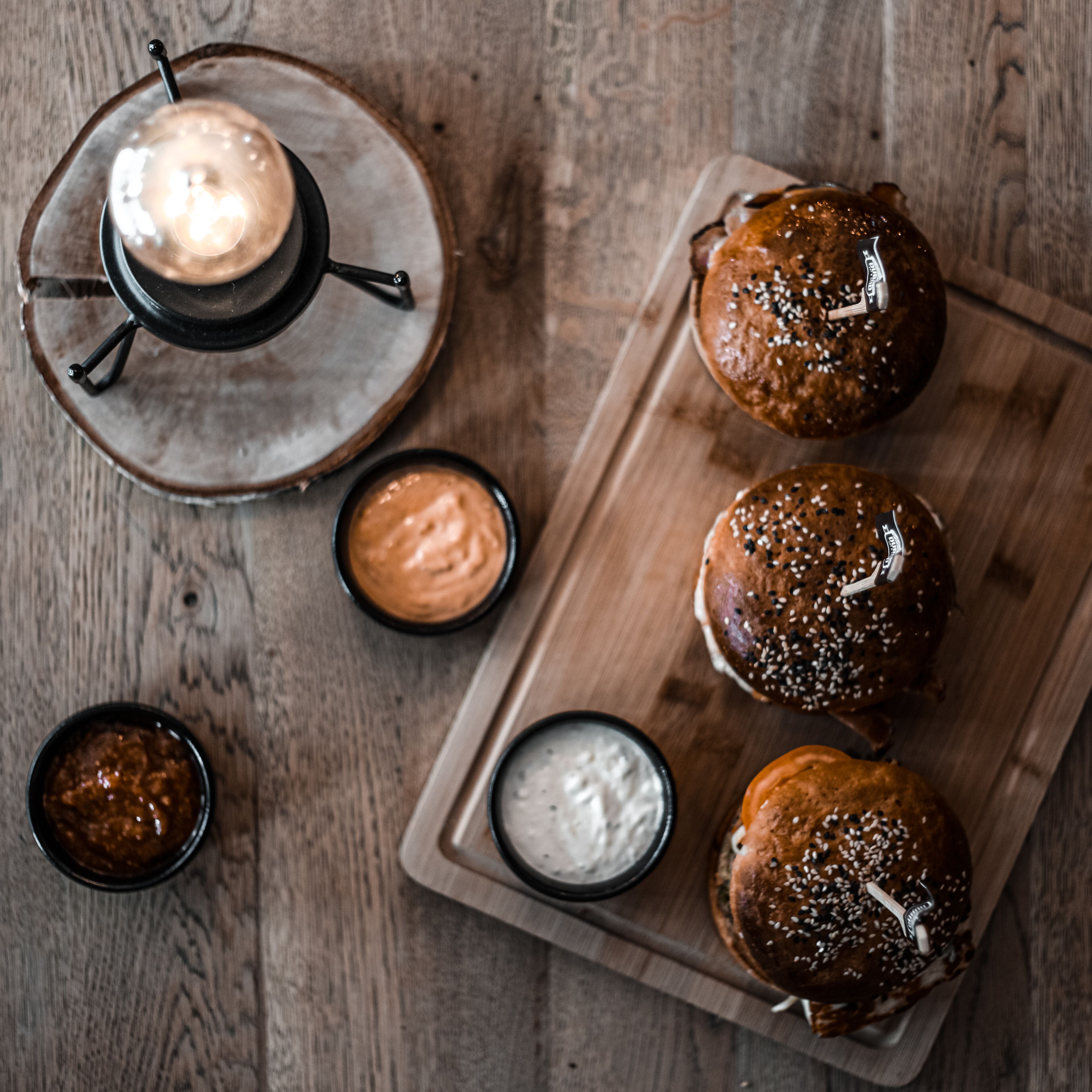 A wooden table with a tray holding four sesame seed buns and three small bowls of sauces.