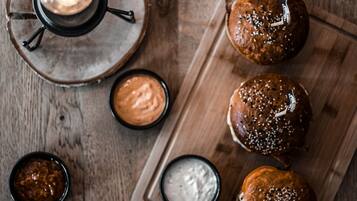 A wooden table with a tray holding four sesame seed buns and three small bowls of sauces.