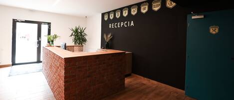 Zona de recepción con mostrador de ladrillo, pared negra con iconos y suelo de madera.