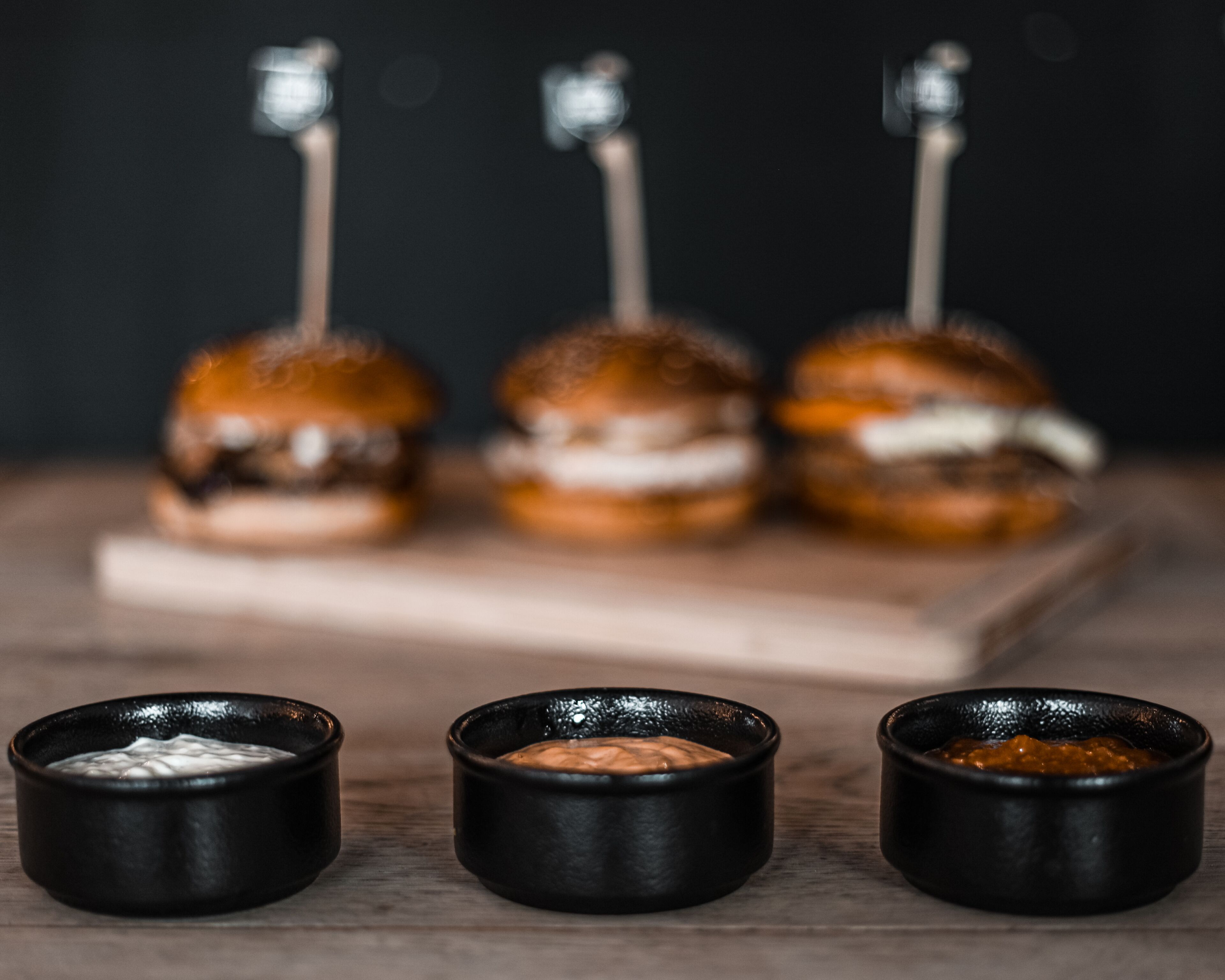 Three skewers of food with three small bowls in front.