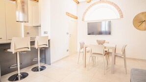 A modern kitchen with a dining area, featuring a large flat-screen TV, a clock, and a rustic archway. - San Giovanni in Valle - Italian Homing (Verona)