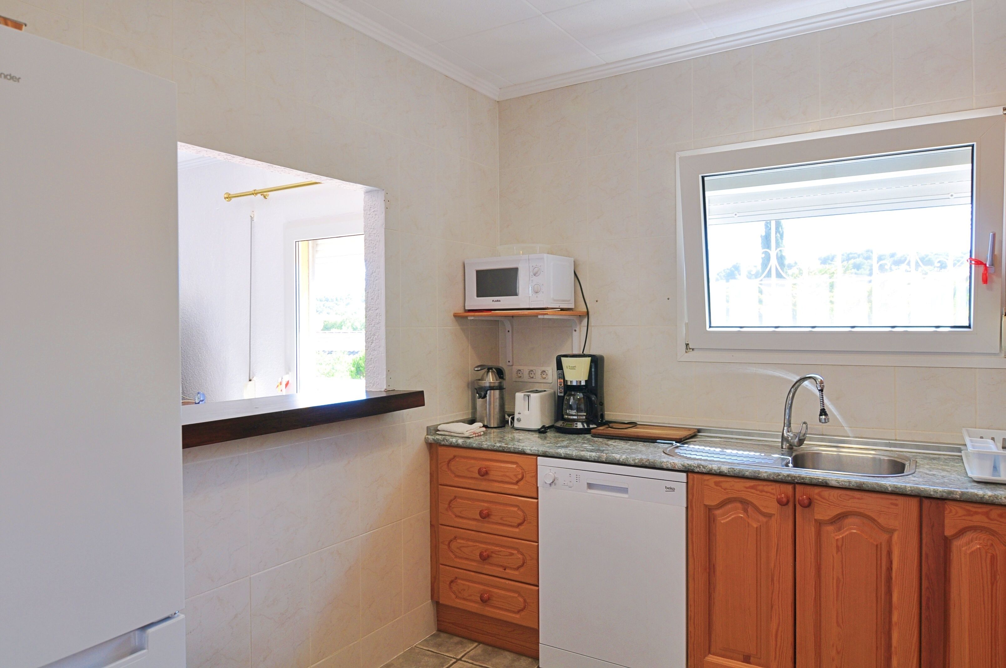 A compact kitchen with a microwave, toaster, and coffee maker on the countertop, wooden cabinets, and a window providing natural light.
